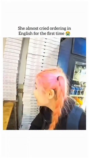humourjoyusa on Instagram: "This short video captures a moment of slight nervousness and ultimate triumph for a young woman with pink hair attempting to order food in English for the first time. The caption notes that "She almost cried ordering in English for the first time." She successfully points to a slice of four-cheese pizza and confidently states, "I want this 4-cheese pizza, one piece," and a can of soda. She struggles slightly when asking for "white sauce pasta," which the counter perso
