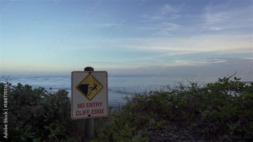 No Entry Cliff Edge drop off sign along Great Ocean Road, calm shoreline and soft evening light as waves roll to shore