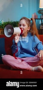Preteen child girl talking with megaphone, proclaiming news, loudly announcing advertisement, warning using loudspeaker to shout speech. Teenager female kid at home evening room apartment on sofa