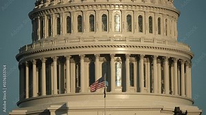 A closeup view of the United States Capitol dome at sunset, showcasing intricate architectural details, including columns, windows, and a statue at the top. Prominent landmark in Washington D.C.