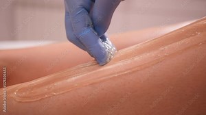 Depilation master woman applying sugar paste on the leg during the procedure of epilation