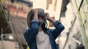 Beautiful woman young asian traveler wearing retro fedora hat using film camera taking a photo at a small street in Bangkok Thailand. Enjoying traveling on holiday summer. Solo travel concept.