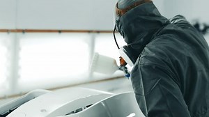 Person applying paint to a car body in a professional automotive spray booth in a workshop