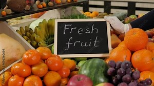A close-up of various fruits in boxes on the shelves in a grocery store, the seller puts a sign next to it with the inscription FRESH FRUITS.