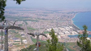 Aerial tramway, sky tram, cable car, ropeway or aerial tram. The cable car cabins suspended on metal ropes move up and down the mountain. At the foot of the mountain overlooks the city of Antalya.