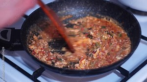 Stirring food in a dark frying pan with a wooden spatula while toasting. Stock full hd video with 25 fps 1080 pixels on the topic of cooking at home on a gas stove.