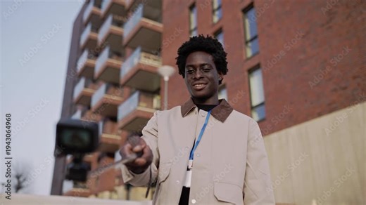 Black male vlogger recording content on a selfie stick outdoors in the city for his social media channel