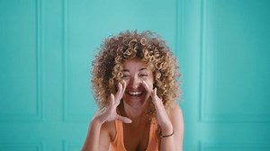 Happy curly young woman shouting in hand loudspeaker, making announcement, excitedly and smilingly announcing and looking at camera