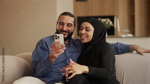 Joyful Arab woman and husband talking with friends during phone video call