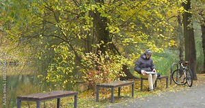 Man With Laptop in Ushanka Hat Freelancer Programmer Copywriter Designer Accountant Stood Up of the Bench Put Laptop into Backpack Got on the Bicycle