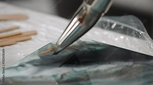 Close-up female artist using construction thermal dryer blowing hot air heating up colorful art epoxy resin on canvas mixing colors into sea waves acrylic painting in art studio, trendy modern hobby