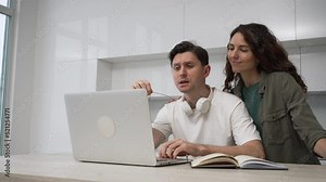 Freelance programmer man with glasses works at home on a laptop, his wife comes up and encourages him to work, massages his shoulders, hugs and kisses.