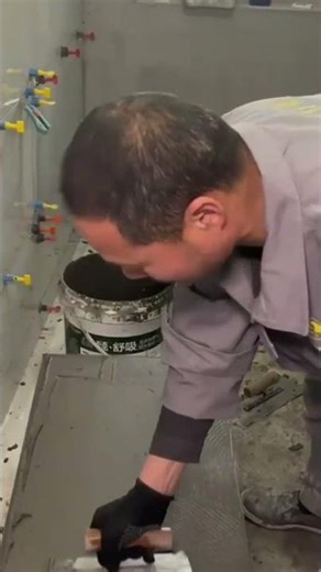 applying the grey adhesive mortar precisely to the back of a large tile using a metal trowel tool