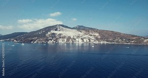 Drone panning view of sailing boats in front the Kaolin quarry in the Mediterranean sea in Lipari, Aeolian islands, Sicily, Italy. Drone is showing a stunning white cliff, beaches and houses.