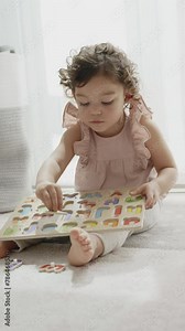 vertical 4k slow motion video of a little girl with curly hair playing sitting on the carpet in her room with a wooden alphabet, Montessori material. Development of concepts and learning in the childh