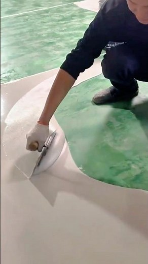 Applying a smooth white epoxy coating evenly across the surface of the green floor