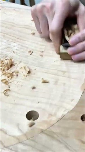 carving and shaping round wooden board surface using sharp hand chisel tool to create smooth curve