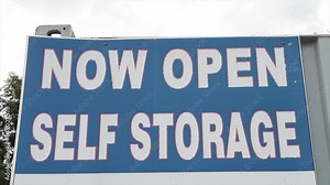 now open self storage sign in white writing caption text against blue background with sky and tree behind Stock Video