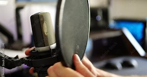 A hand setting up a pop filter for a condenser microphone in a music studio for recording a vocalist podcast or radio show.