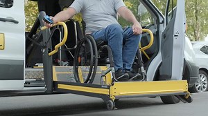 Man using hydraulic lift to board accessible van from sidewalk.