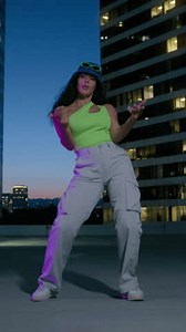 Vertical video. Bottom view sexy woman dancing for camera outdoors at night skyscrapers on background. Cheerful female person moving hands to beat of music at rooftop. Closeup cute girl having fun