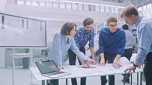 In the Industrial Engineering Facility: Diverse Group of Engineers and Technicians on a Meeting Gather Around Table with Engine Design Technical Drafts, Have Discussion, Analyse Technology