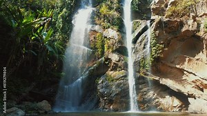Majestic tropical waterfall cascading over rocky cliffs surrounded by lush green foliage in serene natural environment on sunny day. Natural attraction for eco-tourism and outdoor adventure