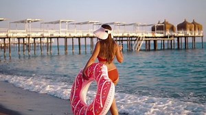 Young woman walking with floating with an inflatable donut circle, back view. She wears hat