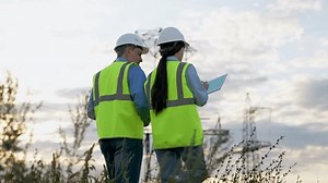 Engineer shows power transmission lines to inspector with tablet at dusk countryside. Engineers with tablet computer discuss power plant maintenance by transmission lines. Electricians in field