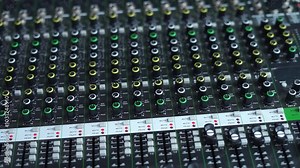 An audio mixer with multiple sliders and knobs being adjusted. The video captures the detailed control of sound levels, perfect for representing audio production, sound engineering, or music creation