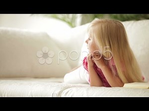 Funny little girl lying on couch with book and smiling. Stock Footage
