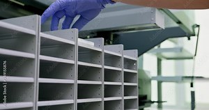 Lab technician placing samples in storage shelves. Gloved hand ensures cleanliness and accuracy in scientific research environment. Laboratory setup designed for organized and sample handling.
