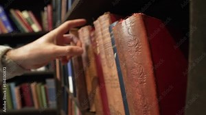 Hand searches across bookshelf, pulling, replacing, and grabbing books they need