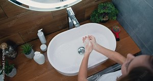 Cute little girl washing her hands with a hand wash gel in sink rinsing with hot water over bathroom sink.