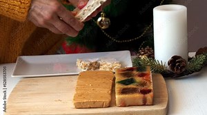 A woman in a yellow knitted sweater breaks a hard almond turron into pieces with her hands.