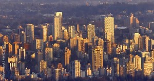 A pan view of Vancouver skyline at sunset. The sky is ablaze with orange, pink, and purple hues, casting a warm glow on the city buildings with lush green trees.