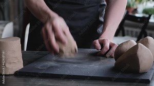 A female sculptor rolls clay with her hands and shapes balls to create ceramics in her workshop. The artist kneads clay for modeling. No face, 4K, 25 frames per second