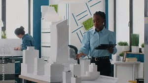 Architect using digital tablet to design layout of building model and maquette in office. Woman engineer working with device to design construction plan for architectural development.