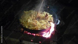 Cooking dinner - fried potatoes in a cast iron skillet on the grill. Stirring with a wooden spatula
