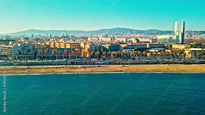 Drone footage of the promenade at La Barceloneta beach with the cityscape in the background.