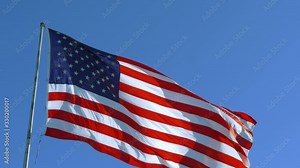 USA American Flag. Looking at flag pole with American flag waving. American Flag blowing in the wind with a blue sky background. 4K video footage.