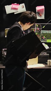 Vertical video Crime expert reads classified case file to uncover new crime details, evaluating evidence authenticity report in police agency office. Inspector working on private investigation