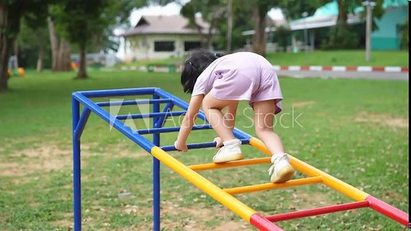 Asian little girl is climbing a ladder on a playground. She is wearing a pink dress and is reaching for the top of the ladder