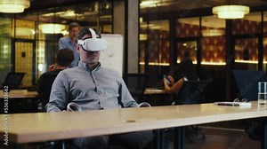 Man using VR headset and wireless controllers, talking online with client, having video call, working in modern office of hi-tech company. Business virtual meeting. Cyberspace digital technology