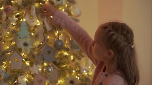 Free stock video - Little girl decorates the christmas tree with balls, lights and ornaments at home