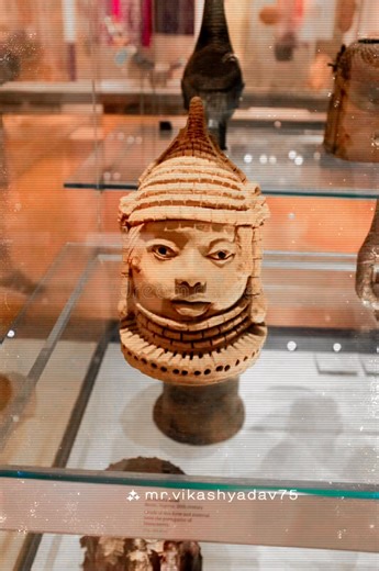 Terracotta head sculpture from Benin, Nigeria, British museum, Uk. Terracotta head sculpture from Benin, Nigeria, dated to the 20th century, displayed in a glass case. The artwork features intricate details with a patterned headdress and expressive facial features, embodying traditional Benin artistic styles. The sculpture rests on a cylindrical base, showcasing craftsmanship in textured terracotta material. The museum setting provides an educational context, highlighting African cultural and hi