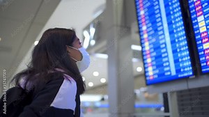 Close up head shot woman in medical mask stand in front of airline time schedule board, at airport terminal, travel during covid-19 pandemic, new normal lifestyle social distance, blue led screen