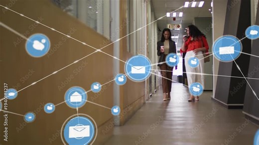 Two women walking office hall, one speaking into phone causing blue icons forming web around them