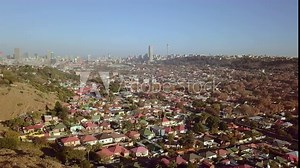 Wide aerial tracking shot of Joburg suburban houses and Johannesburg city landscape as backdrop. Early morning.