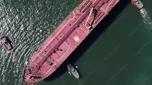 Top down view of Tug boats assisting big cargo ship. Large cargo ship enters the port escorted by tugboats.